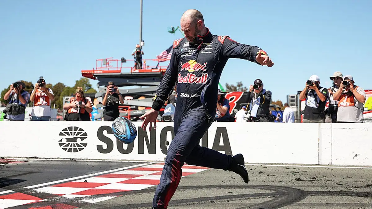 Shane Van Gisbergen kicking a rugby ball at Sonoma Raceway.