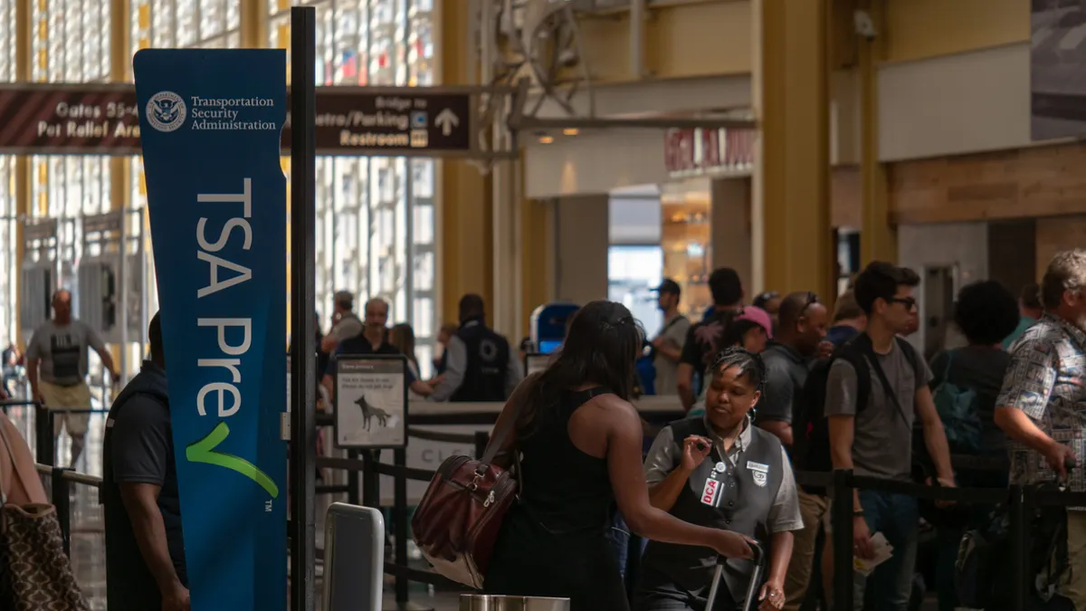 Travelers move through a TSA PreCheck security lane at an airport checkpoint.