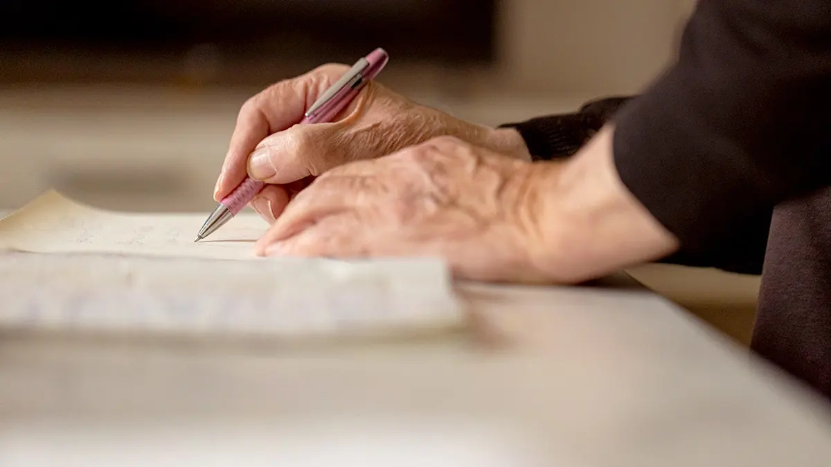 Senior man writing in an old notebook with a pen.