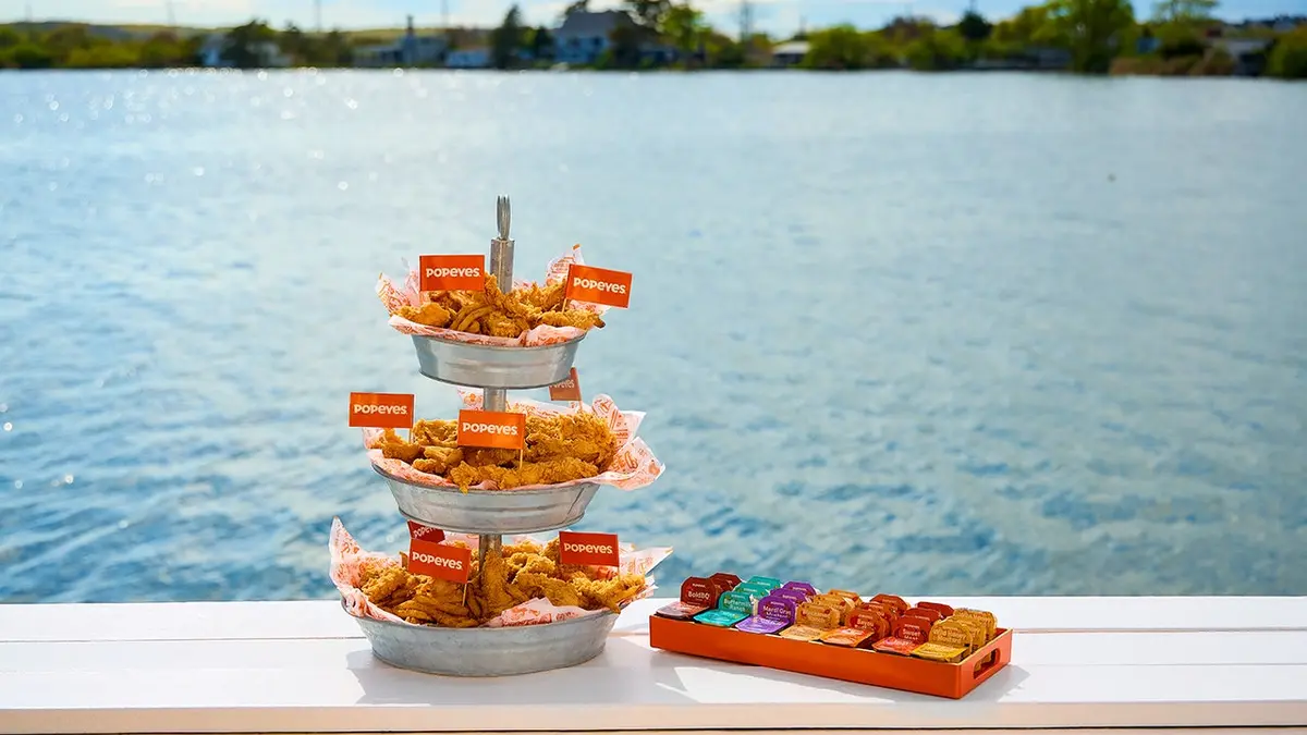 Popeyes' chicken tender tower sits on a deck in front of a body of water.
