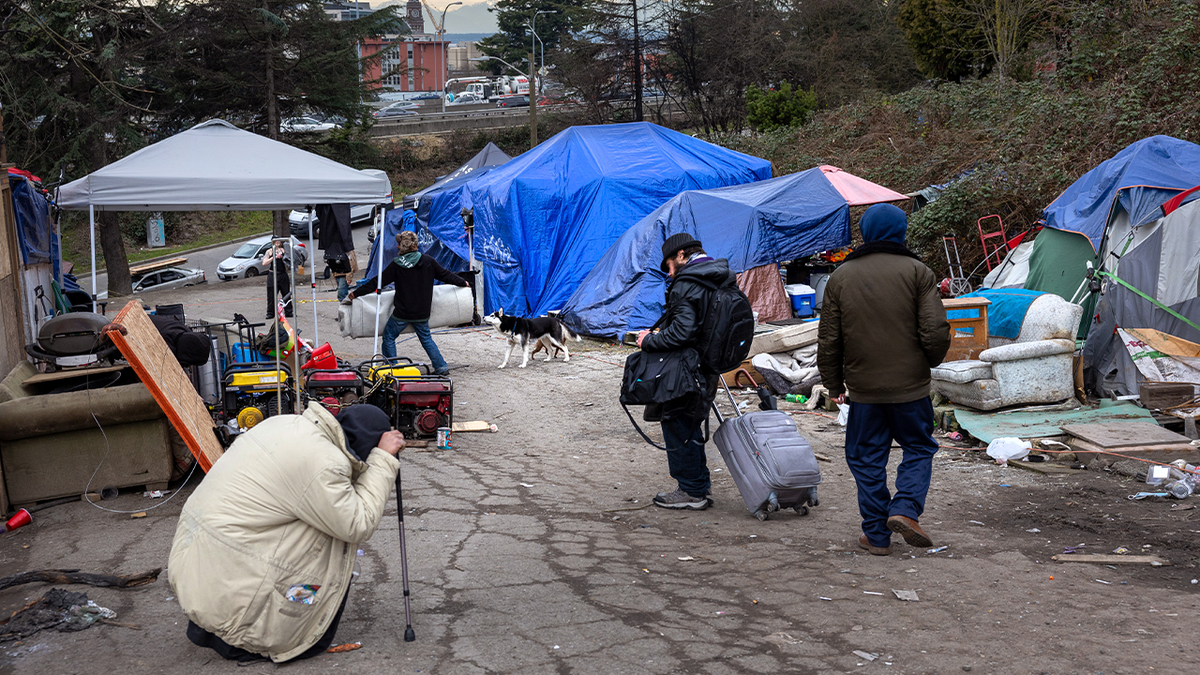 Residents walking through a homeless encampment with tents and belongings in Seattle