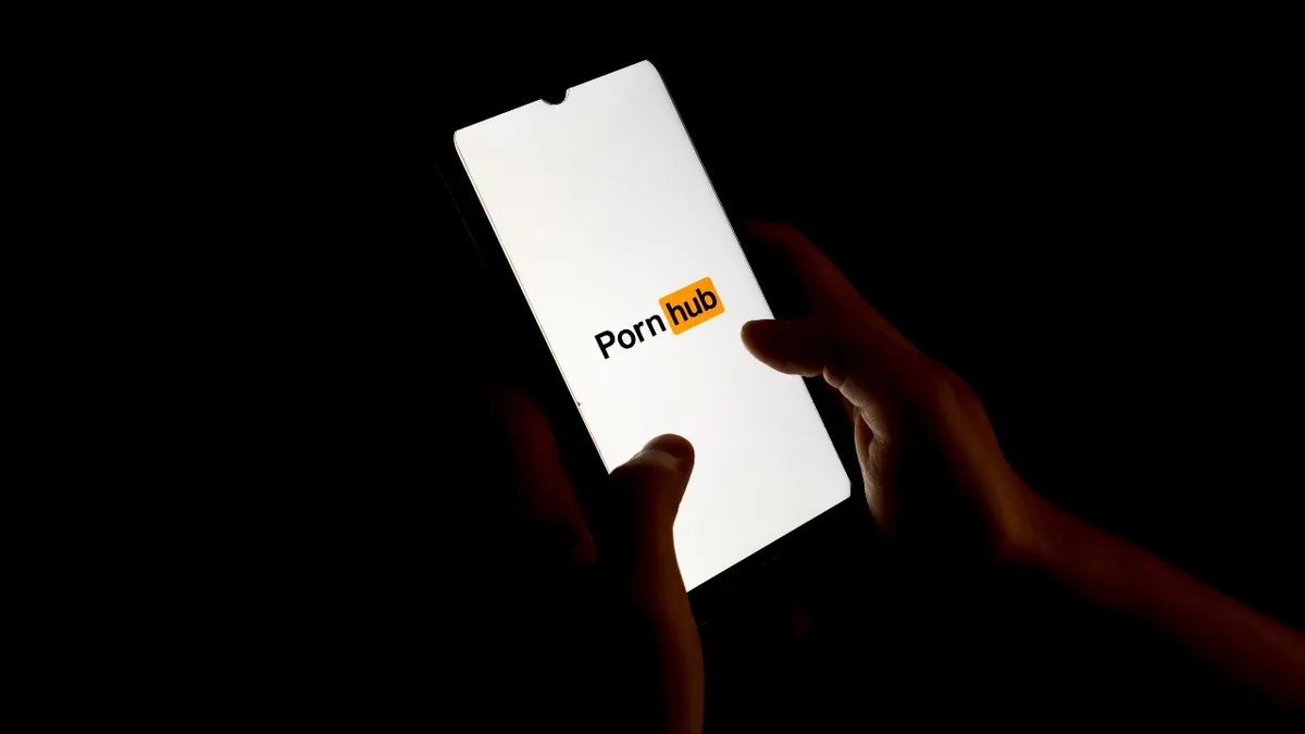 Kristy Althaus holding a smartphone displaying the PornHub logo