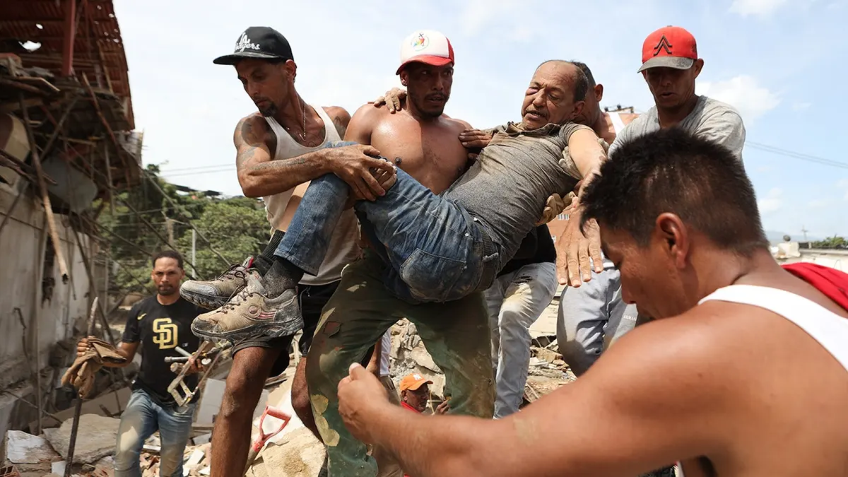 Neighbors carrying a man rescued from rubble of collapsed building in La Guaira