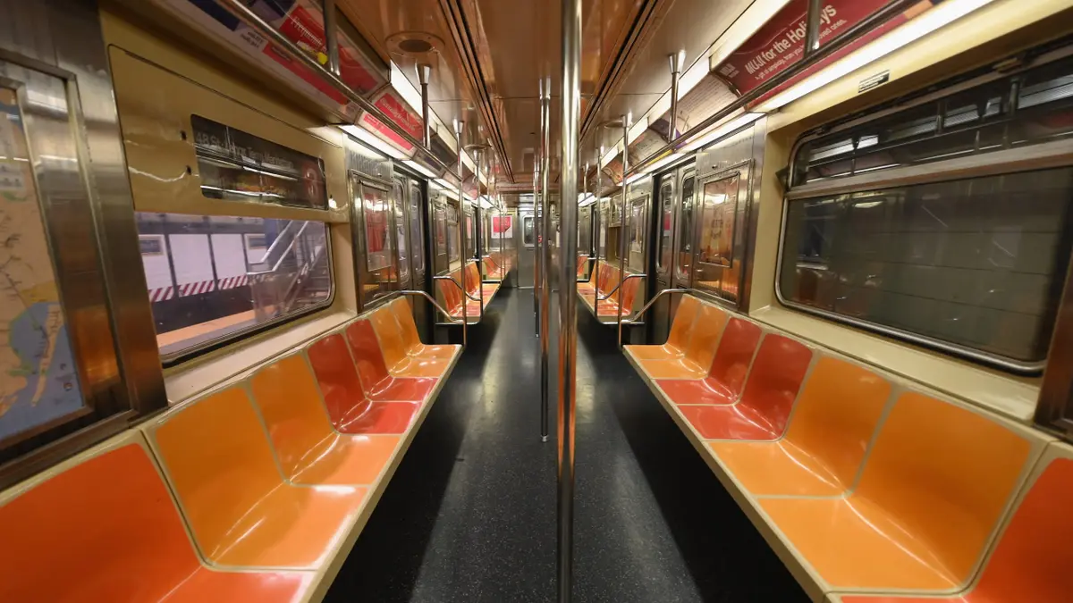 An empty New York subway car interior with rows of seats and handrails.