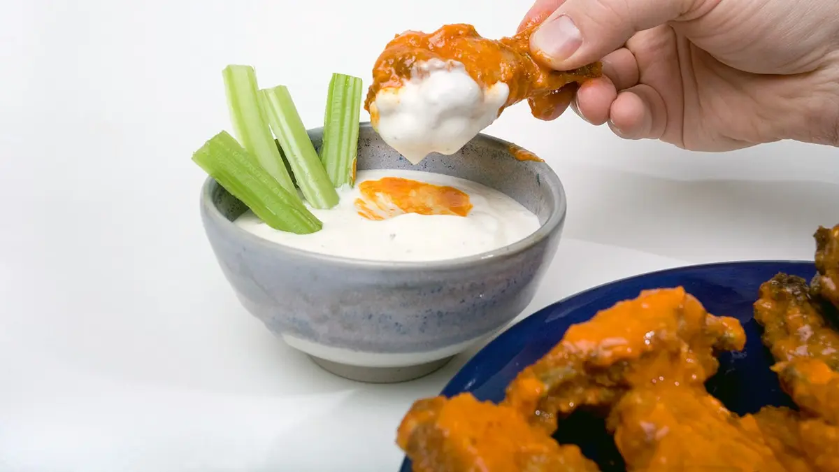 Hand dipping a wing into ranch dressing