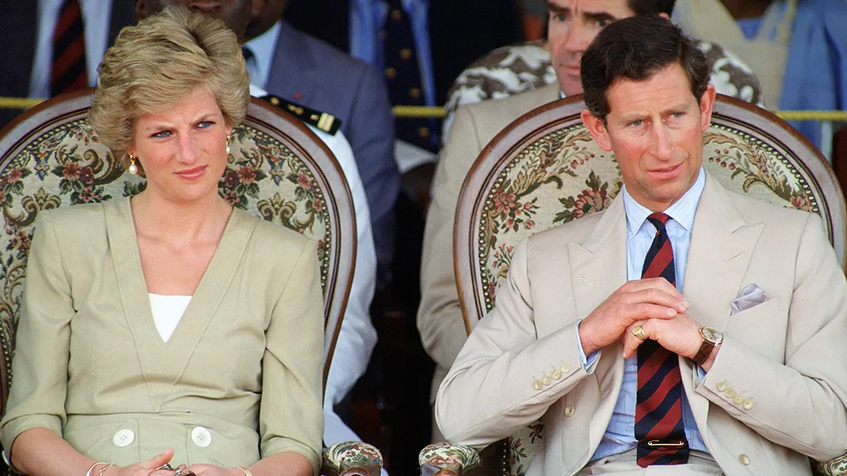 Prince Charles and Princess Diana standing outdoors wearing matching tanned suits.