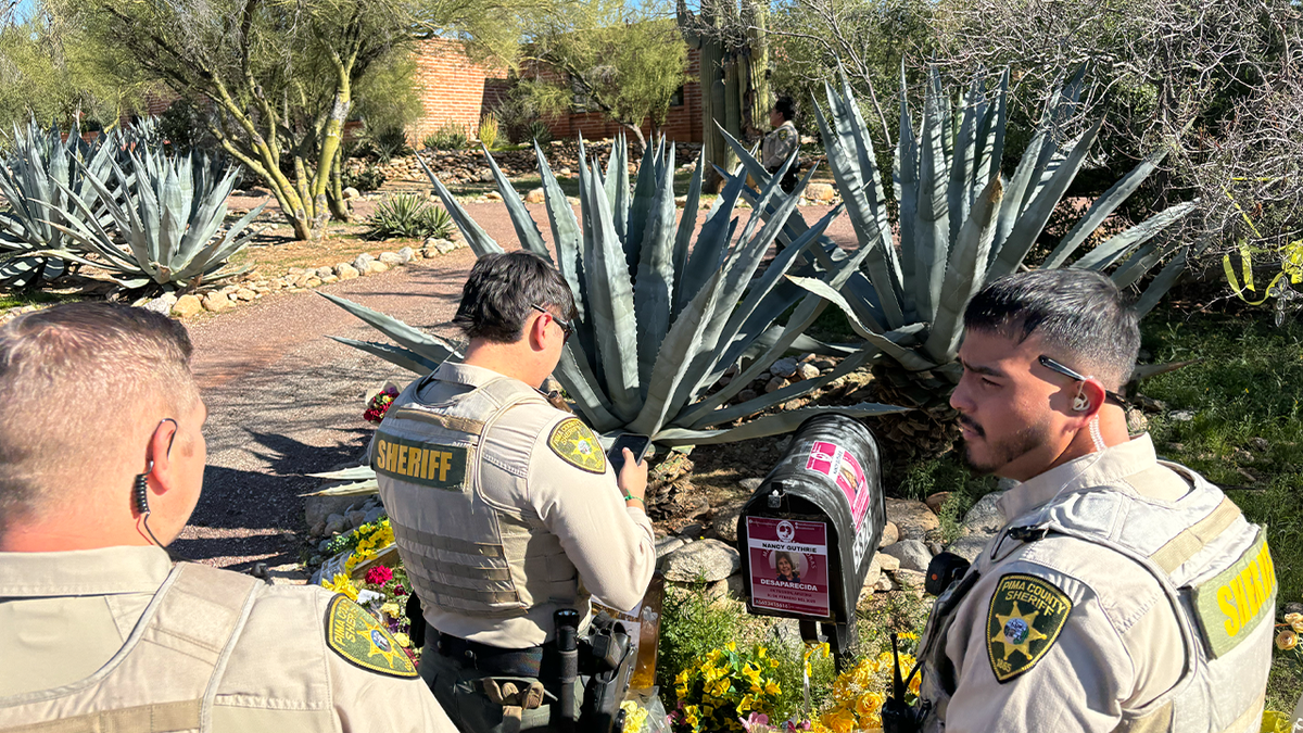 Pima County deputies examine a flyer taped to the mailbox at Nancy Guthrie's home in Tucson, Arizona, on Feb. 23, 2026. Guthrie, the 84-year-old mother of