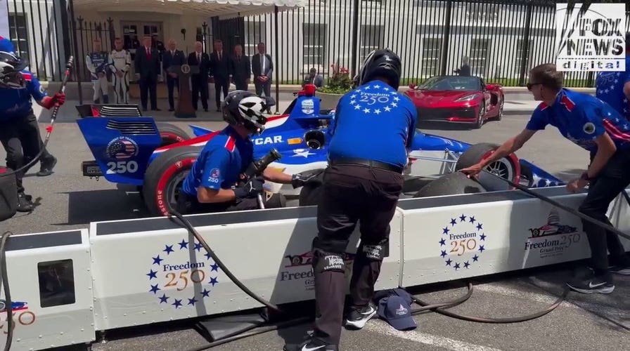 An IndyCar driver zooms toward pit crew at preview of America 250 Grand Prix.