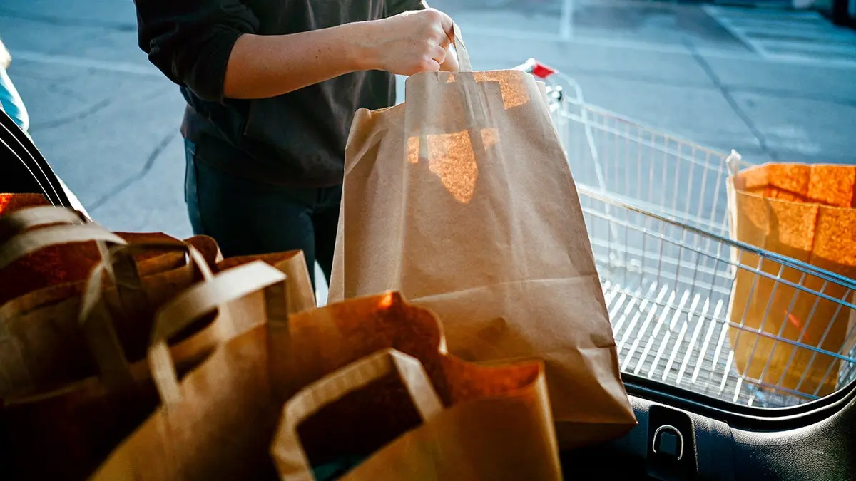 A person takes bags of groceries out of the back of a car.
