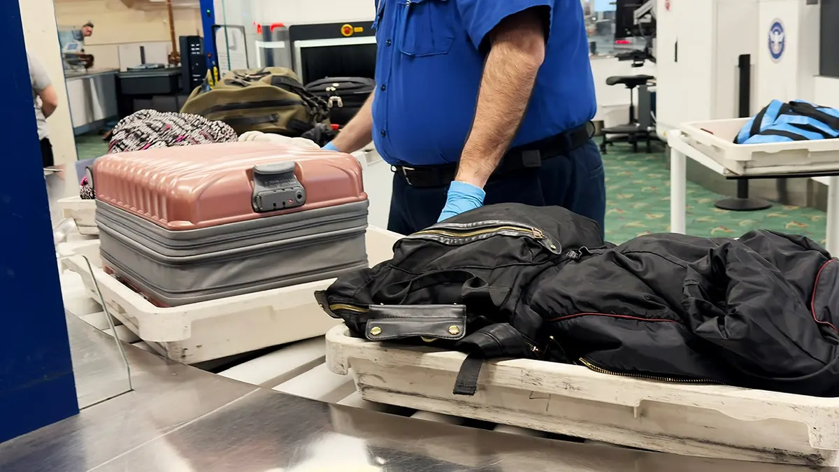 Travelers move through an airport TSA security checkpoint with luggage.