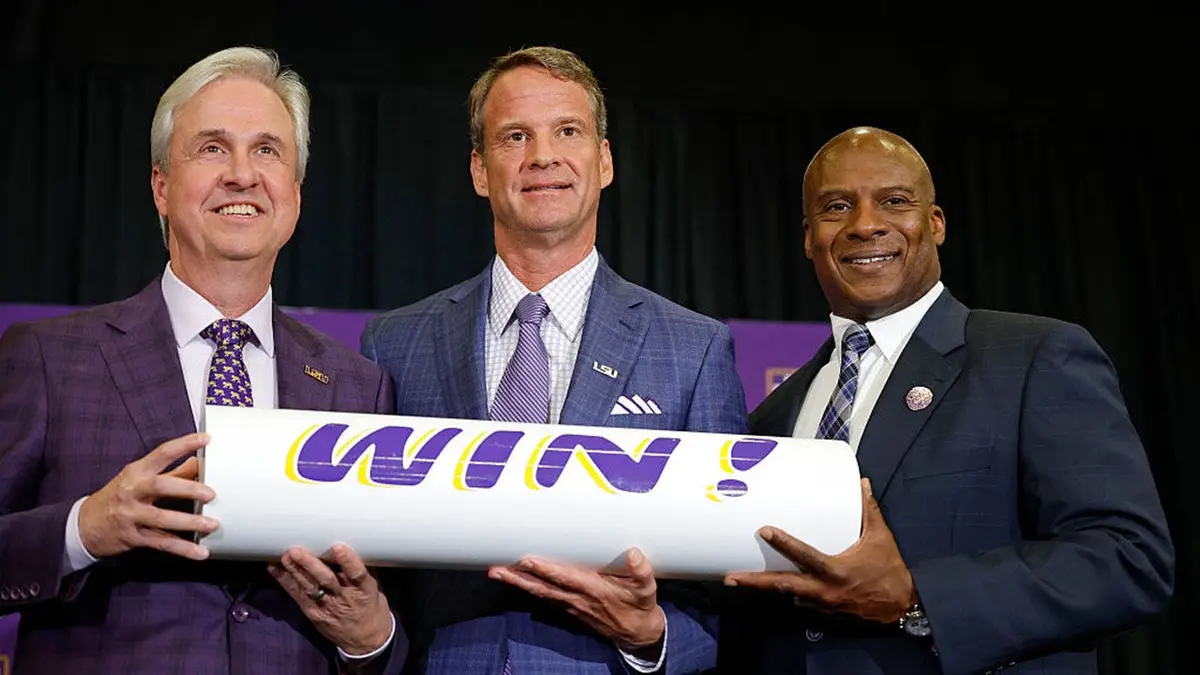Lane Kiffin poses with LSU President Dr. Wade Rousse and interim athletic director Verge Ausberry at a press conference.