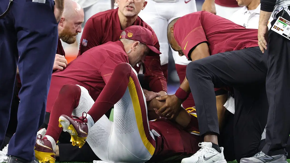 Jayden Daniels lies on the field with an apparent left arm injury during an NFL game.