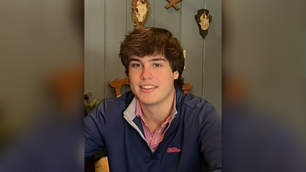 Robert Strang in an Ole Miss pullover poses for ap ortrait in front of a green wall