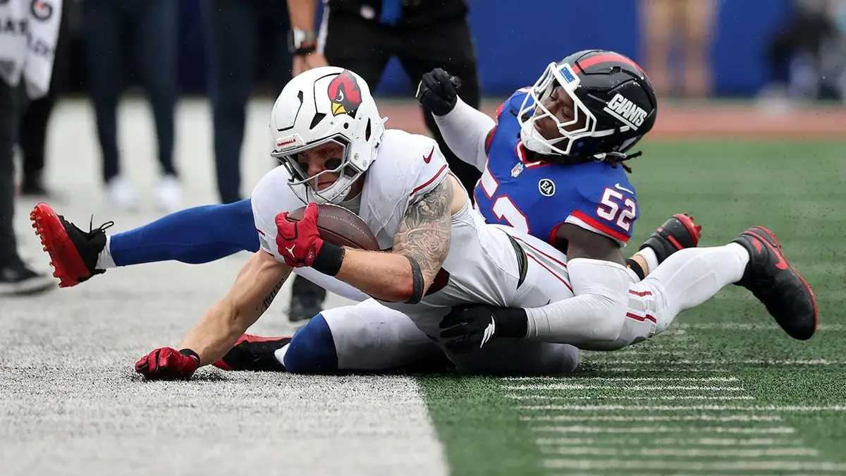Arvell Reese #52 of the New York Giants tackles Trey McBride #85 of the Arizona Cardinals during an NFL game.